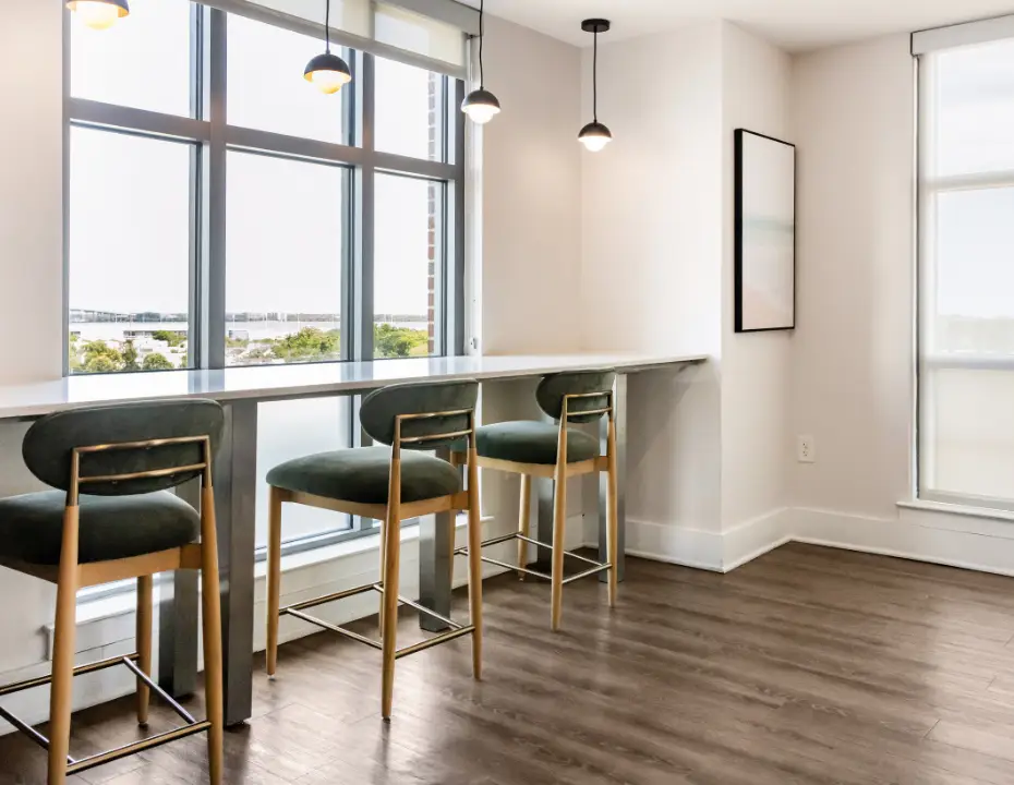 Window-side coworking bar with upholstered stools, pendant lighting, and expansive city views.