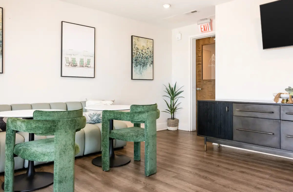 Website I Modern resident lounge featuring green upholstered seating, round tables, contemporary artwork, and a media console with TV.