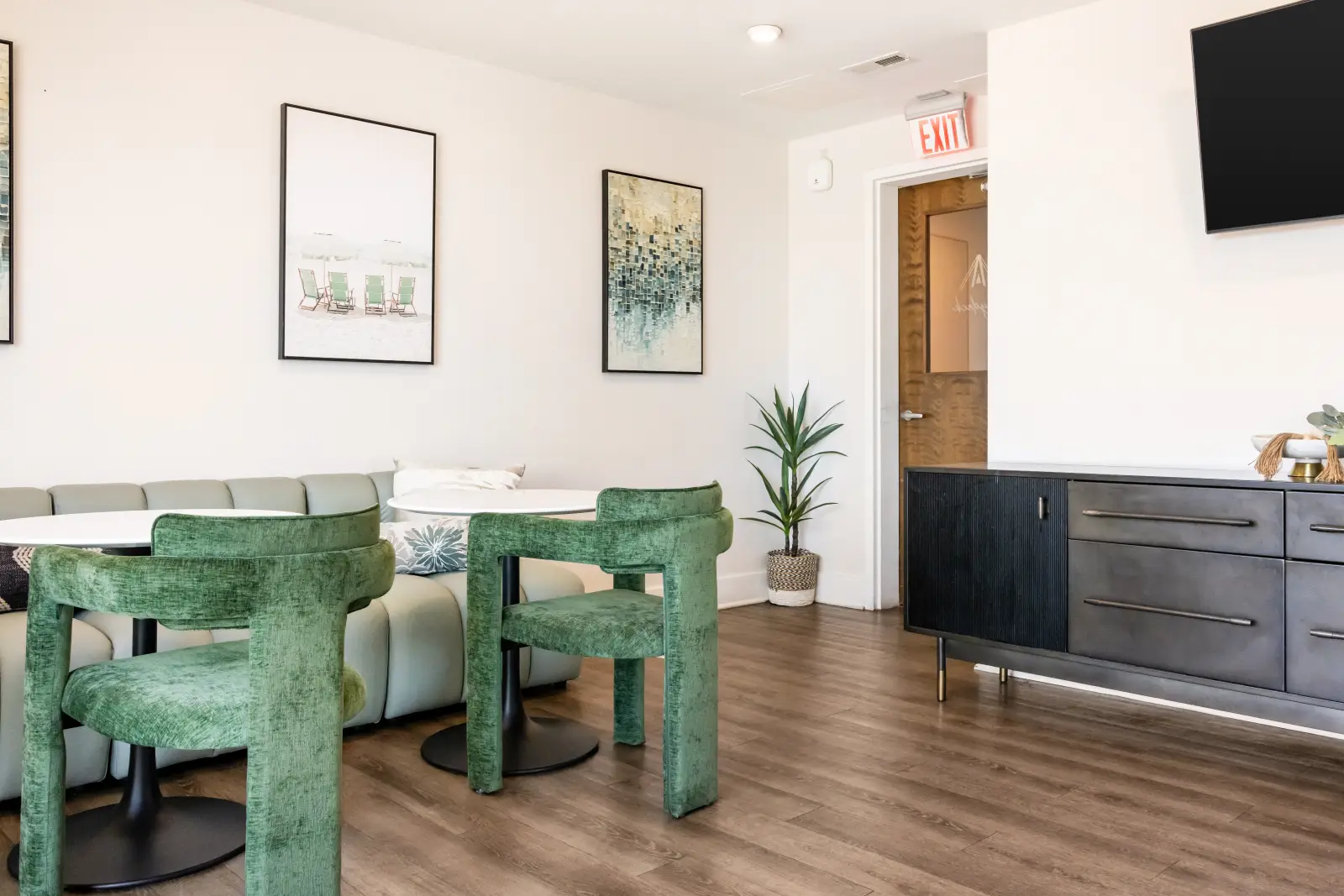 Modern resident lounge featuring green upholstered seating, round tables, contemporary artwork, and a media console with TV.
