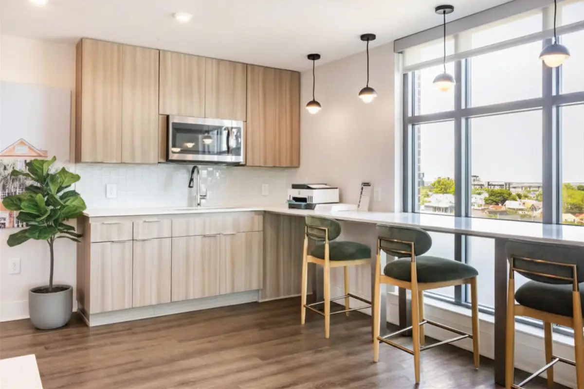 Resident lounge kitchenette with light wood cabinetry, bar seating, pendant lighting, and floor-to-ceiling windows.